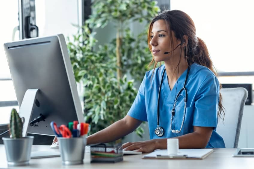 Nurse at desk telehealth office Shot of female doctor talking with earphone while explaining medical treatment to patient through a video call with computer in the