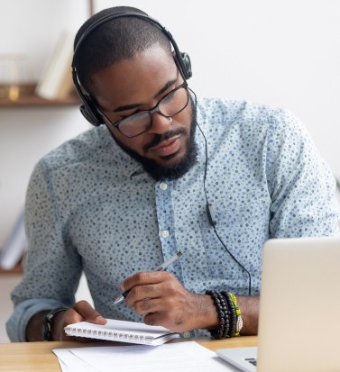 Laptop headphones african man webinar (2) Focused african business man in headphones writing notes in notebook watching webinar video course, serious black male student looking at laptop listening lecture study online on computer e learning (Focused african business man in headphones writing